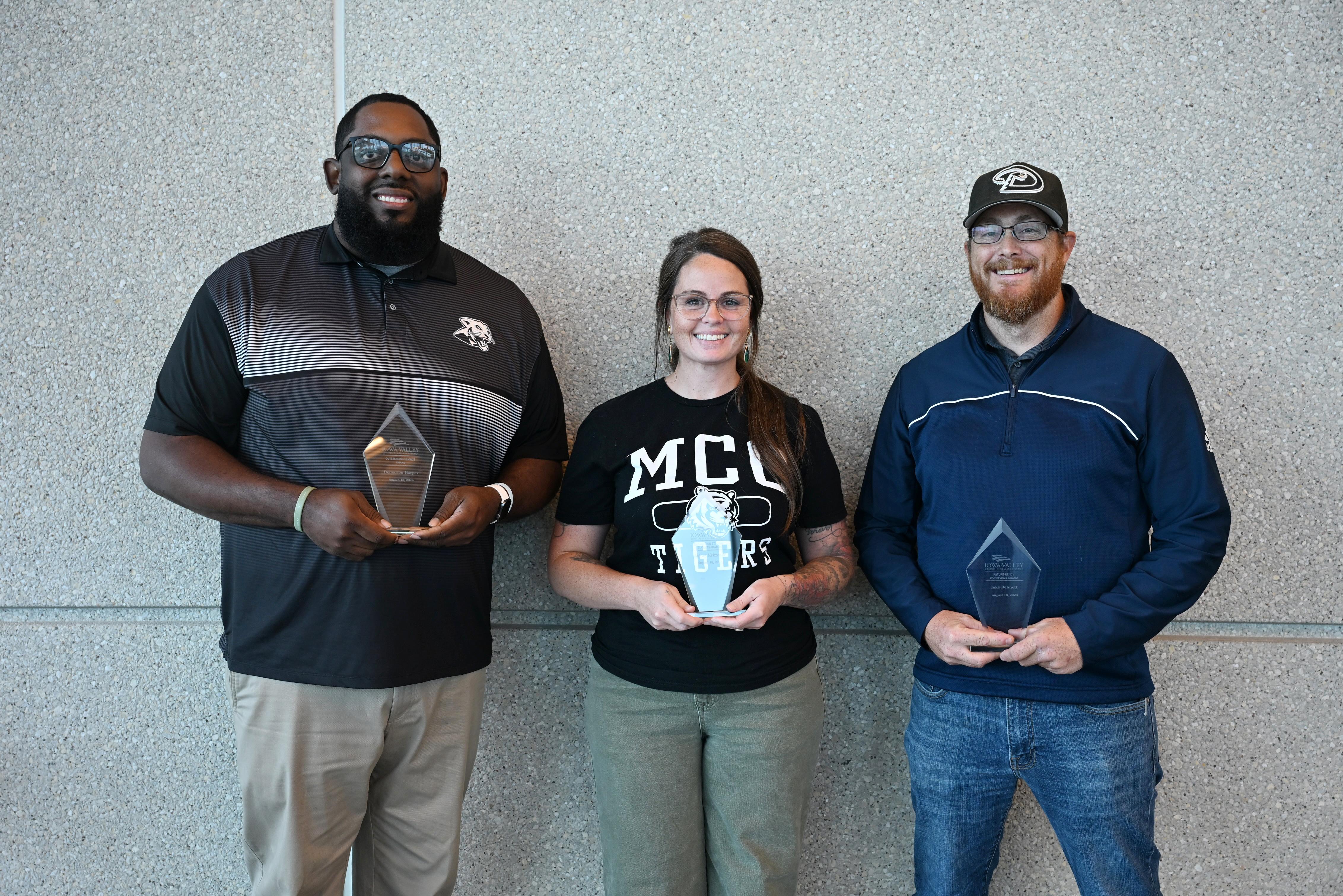 Three award recipients stand side by side in front of a textured wall, each holding a glass recognition plaque during an employee awards event.