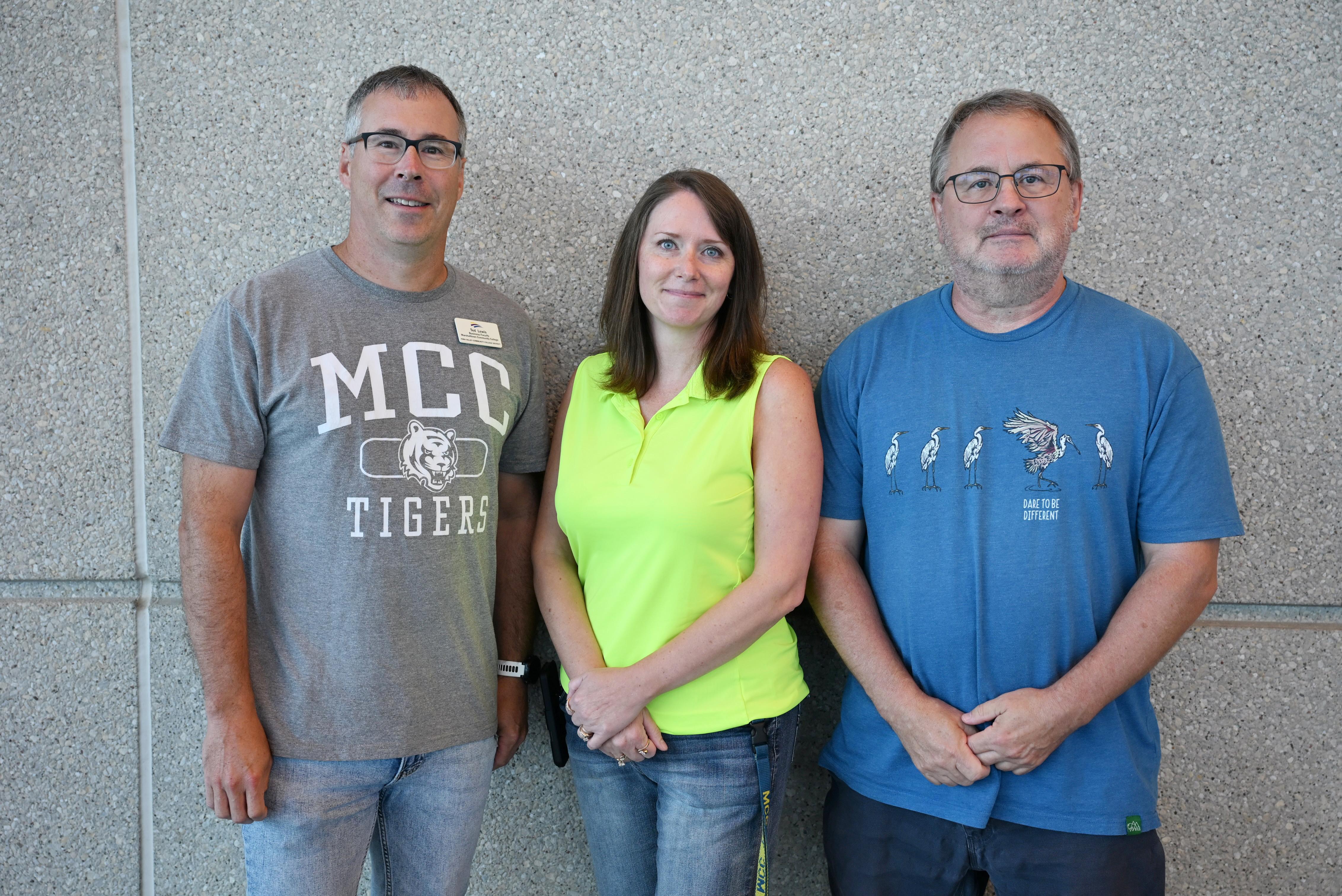 Three employees stand together in front of a textured wall during a workplace recognition event.