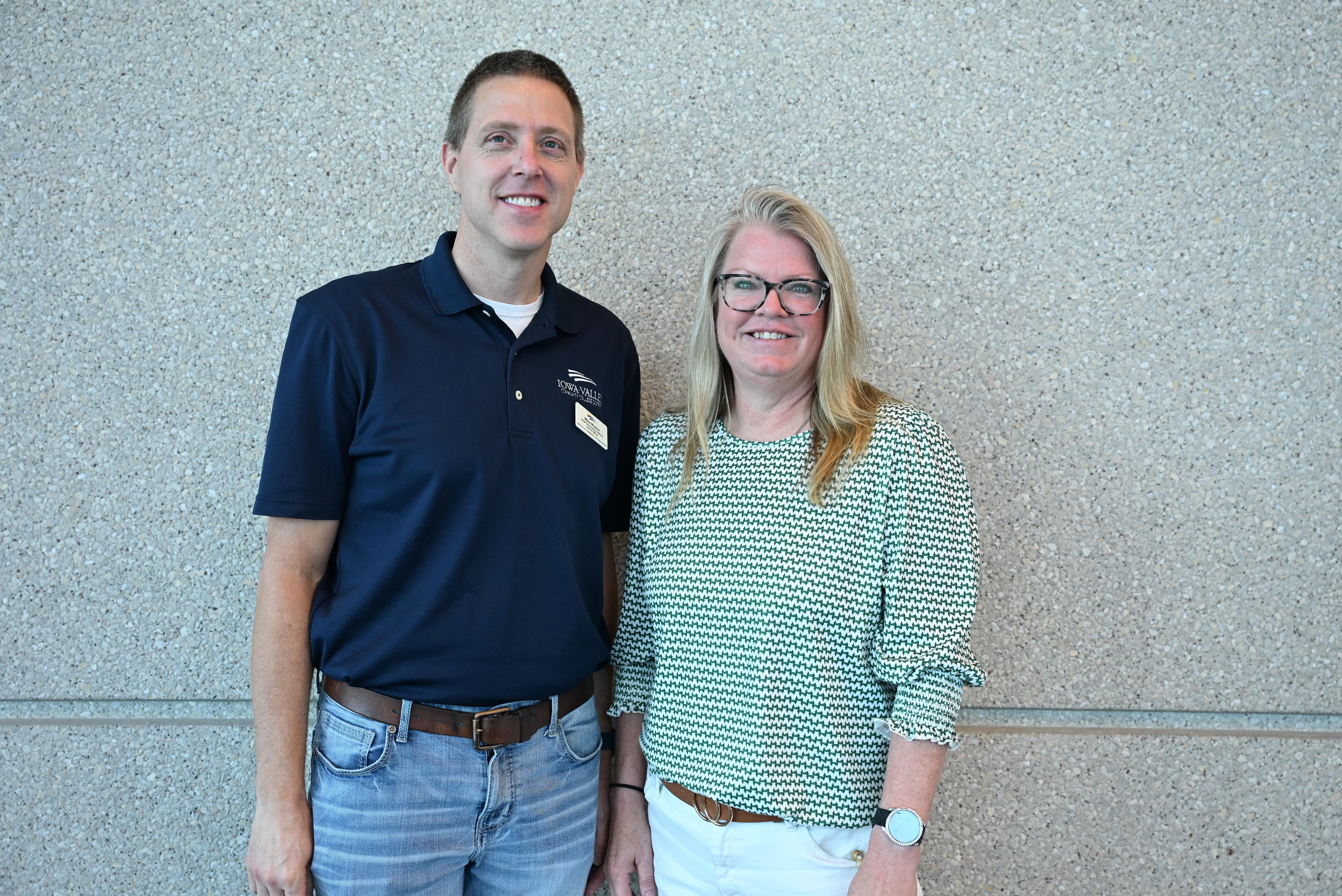 Two employees stand together in front of a textured wall for a workplace recognition photo.