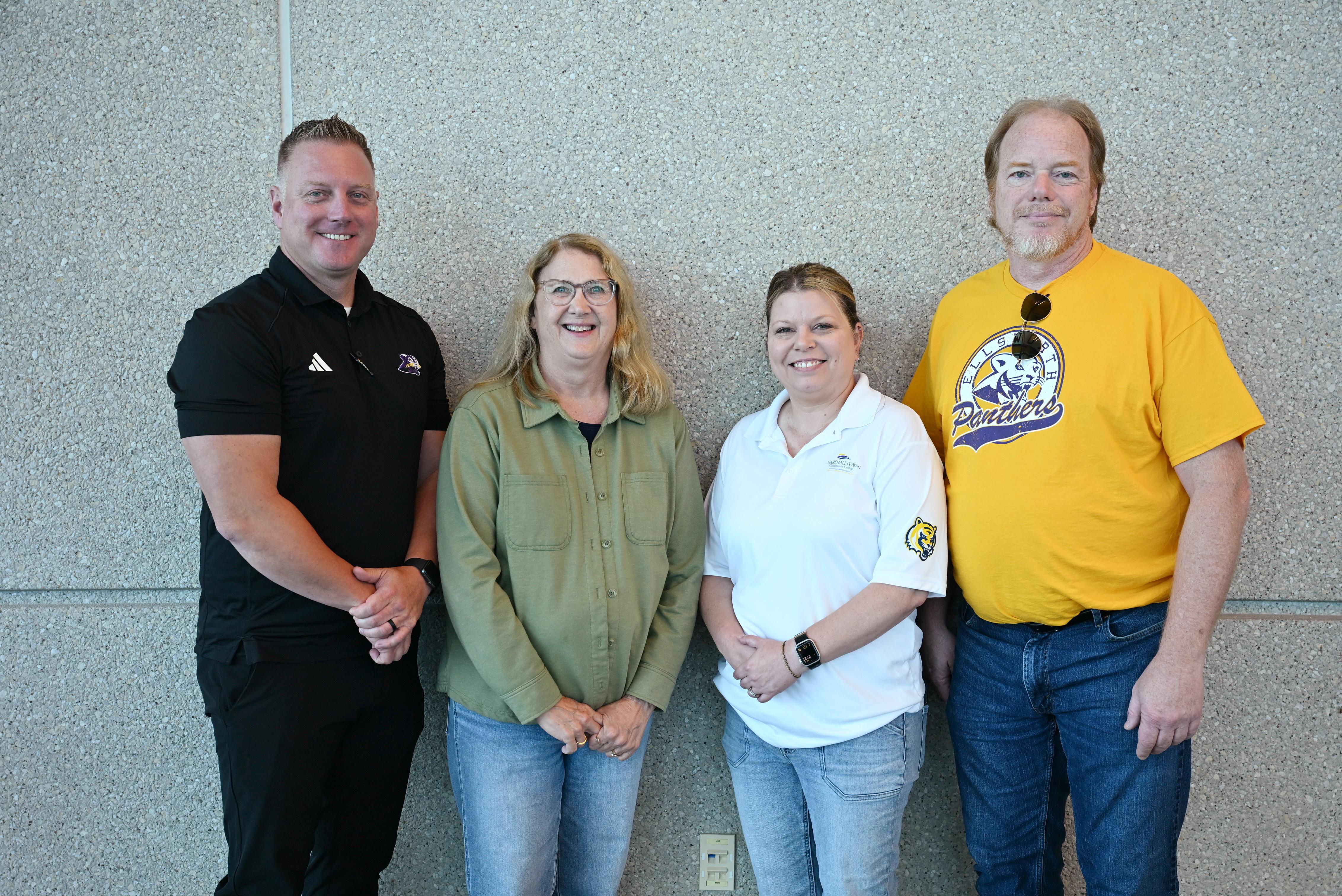 Four employees stand together for a group photo in front of a textured wall during a workplace recognition event.