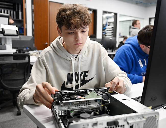 Computer Network Management male student working on the inside of a computer
